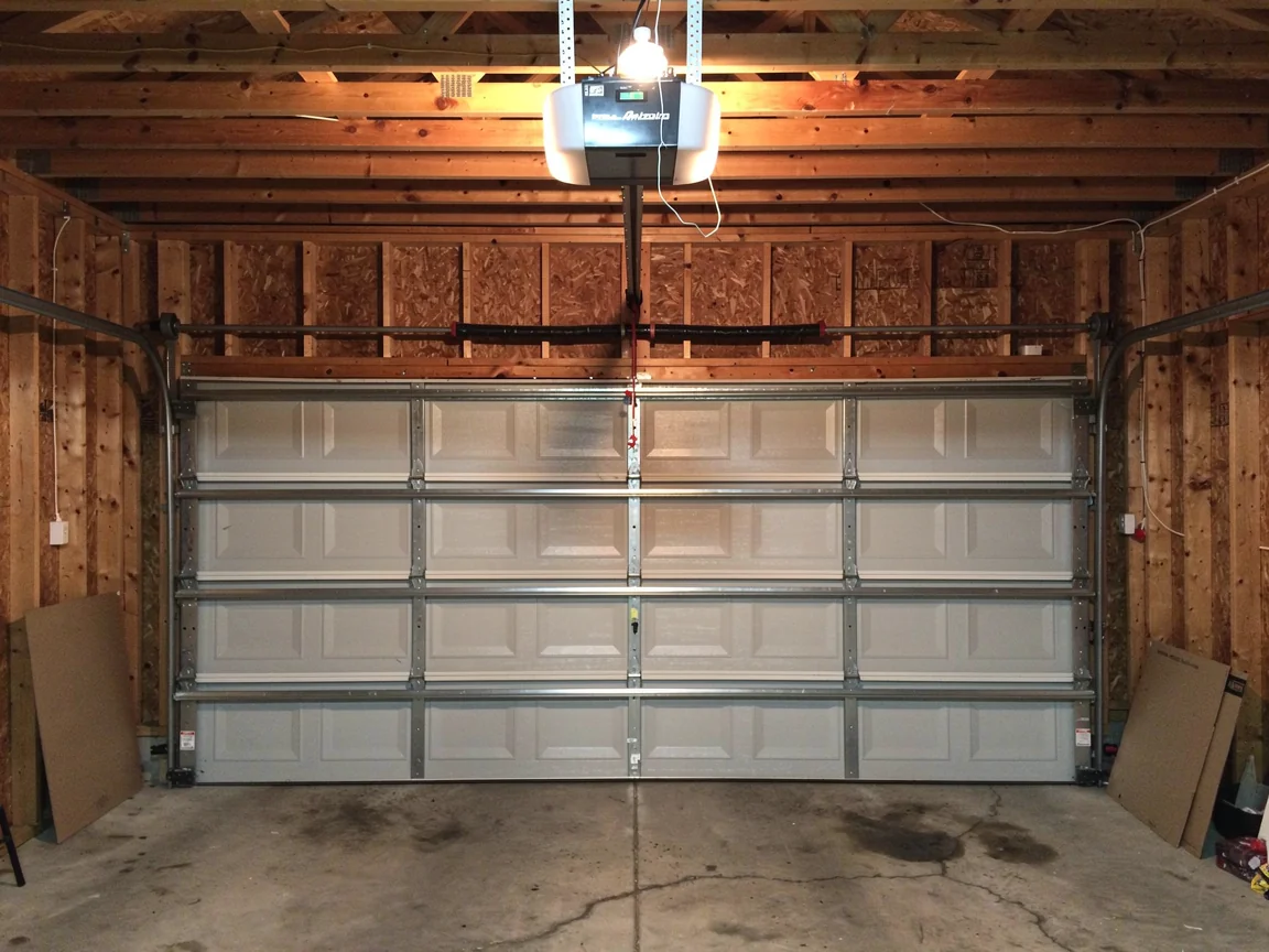 A closed white garage door is visible from inside a garage with wooden walls.